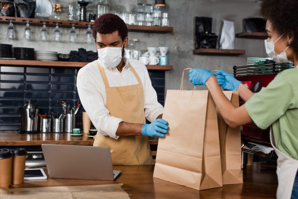 Work at a cafe hands paper bags to someone across a counter.